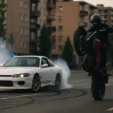 Voiture effectuant un drift et moto réalisant un wheeling en pleine ville, illustration d’une manœuvre acrobatique et d’une conduite dangereuse sanctionnées par le Code de la route