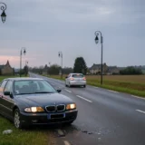 Délit de fuite : véhicule accidenté sur le bas-côté avec débris sur la chaussée tandis qu'une voiture s'éloigne à l'horizon
